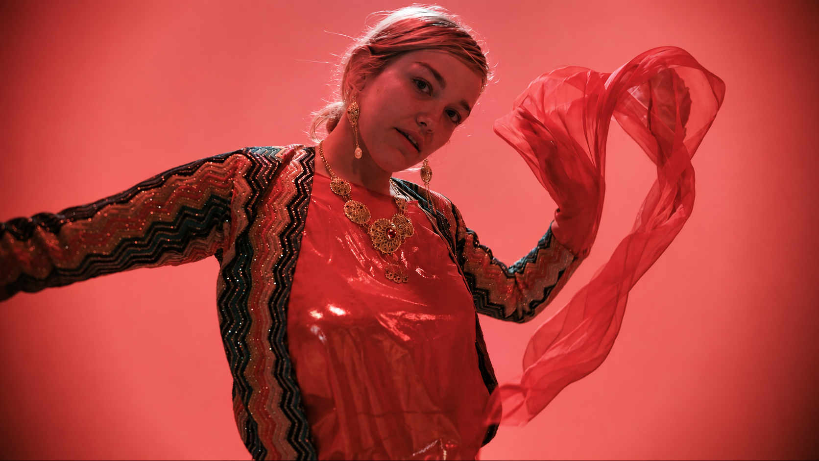 Performer in traditional dress holding a flowing scarf under red lighting